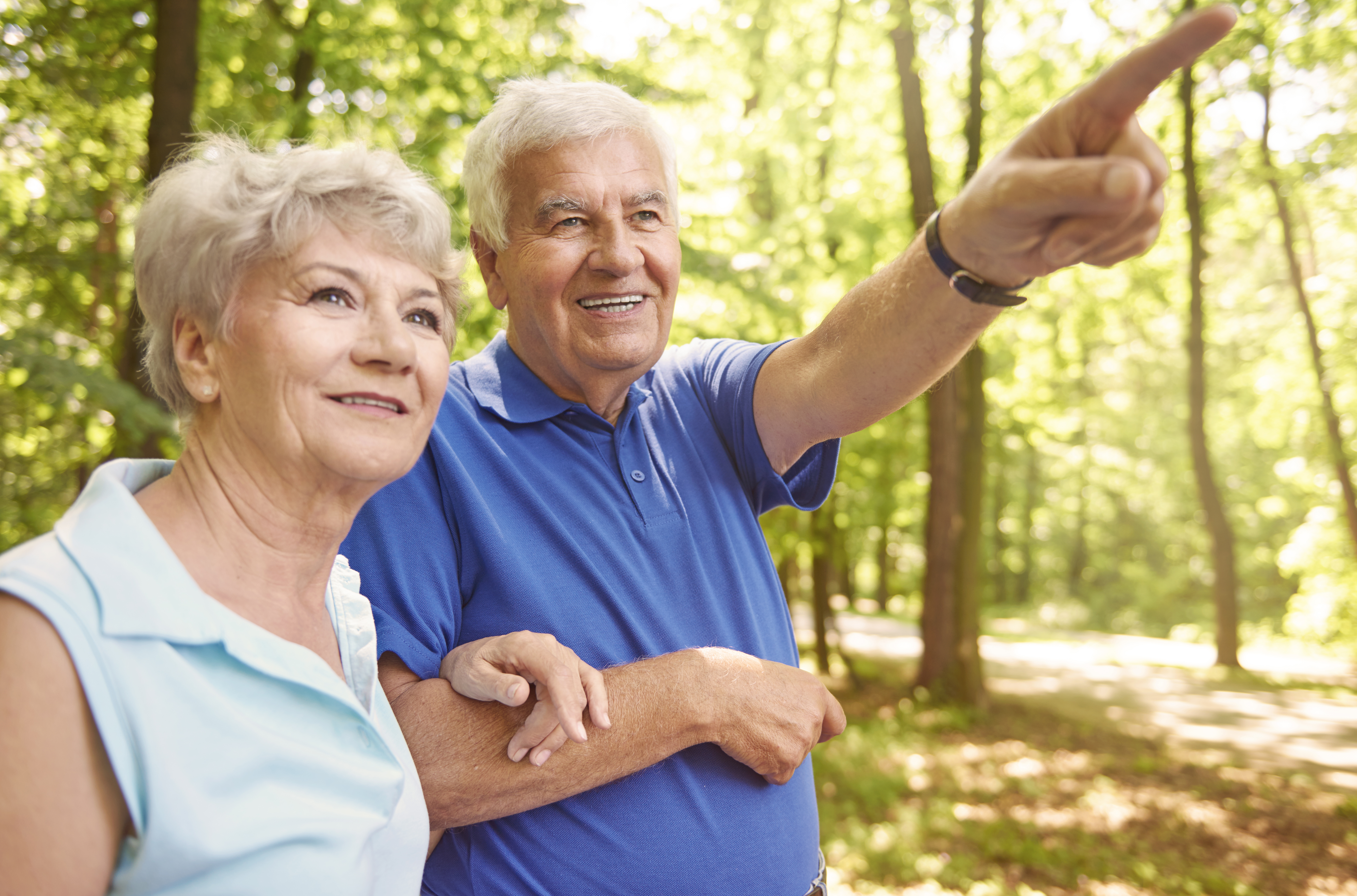 Senior i&nbsp;seniorka w&nbsp;lesie. Senior wskazuje palcem na&nbsp;coś, czego nie widać na&nbsp;obrazku