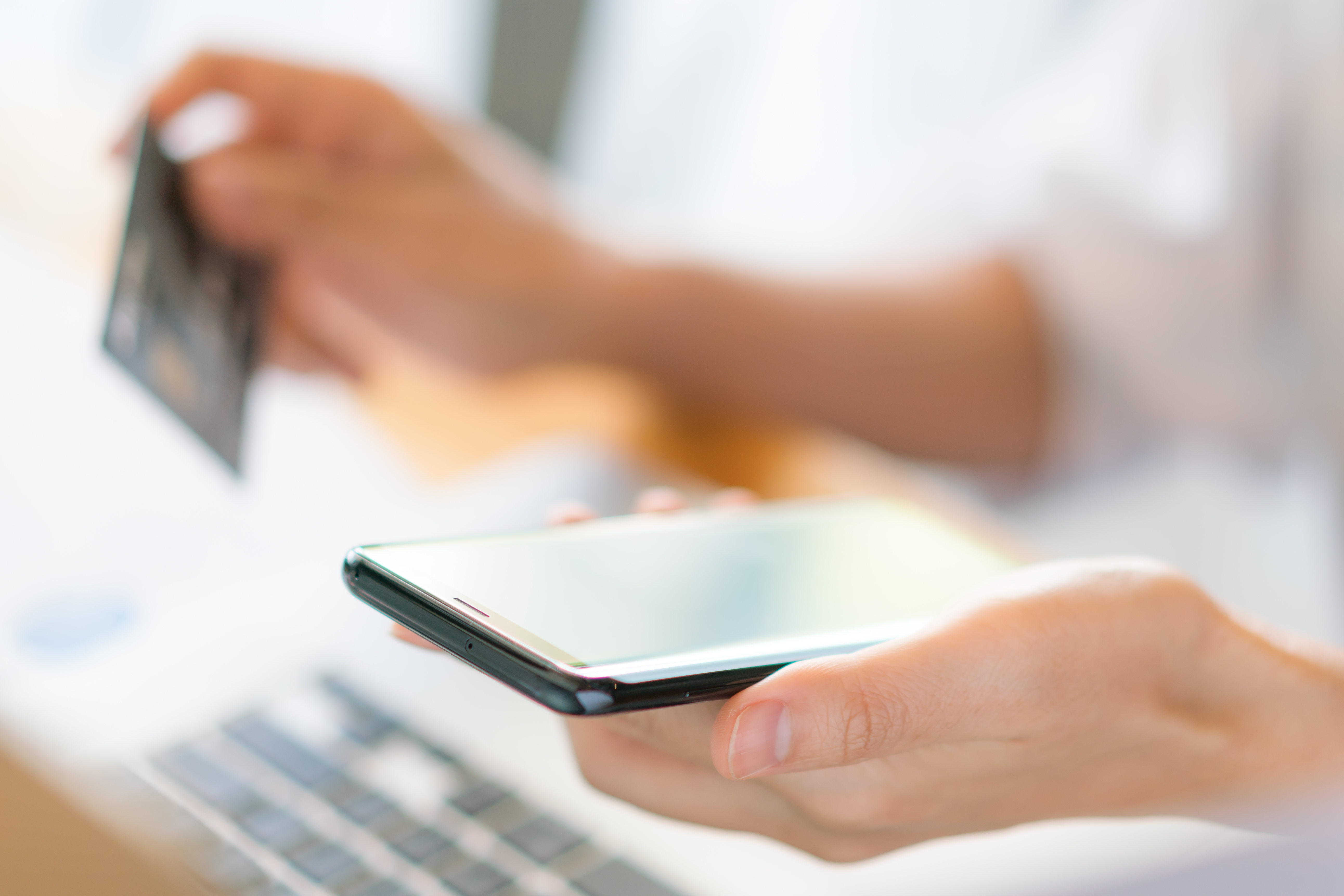 Kobieta trzymająca w&nbsp;rękach telefon i&nbsp;kartę płatniczą